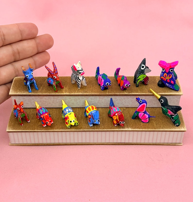 K&ouml;nnte beinhalten: Eine Sammlung von vierzehn kleinen, handbemalten Tierfiguren aus Holz, die auf einem zweistufigen St&auml;nder angeordnet sind. Die Miniaturfiguren weisen lebendige, mehrfarbige Muster auf, darunter Streifen, Punkte und florale Motive.