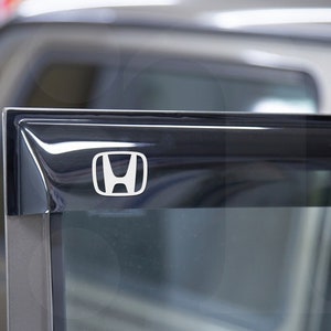 May include: Close-up of a black car door with a silver Honda logo. The logo is a stylised "H" with a curved line on each side.
