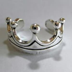 May include: Silver crown ring with a textured design. The ring is open and adjustable.