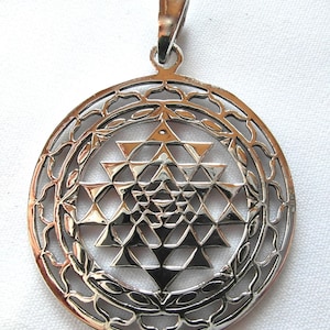 May include: Silver pendant featuring a Sri Yantra, a sacred geometric symbol in Hinduism, with a detailed, intricate design. The pendant is circular and has a delicate, ornate border.
