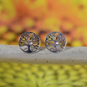 Op de afbeelding: Een paar zilveren oorbellen met een boom des levens. De oorbellen zijn rond en hebben een gedetailleerd boomontwerp met een kleine cirkel in het midden.