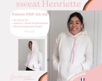 Puede incluir: Una sudadera con capucha blanca con un cordón rosa. La sudadera está puesta en una modelo y el texto "niveau débutant" es visible en la esquina inferior derecha de la imagen. El texto "sweat Henriette" es visible en la parte superior de la imagen.