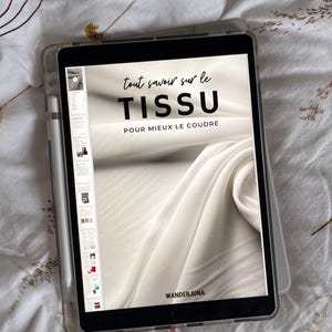 Może przedstawiać: Biały tablet w przezroczystym etui, na którym wyświetlana jest cyfrowa okładka magazynu z tytułem "tout savoir sur le TISSU POUR MIEUX LE COUDRE" i tekstem "WANDERJUNA" na dole.