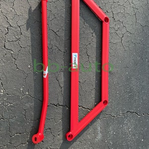 May include: Two bright red automotive chassis braces. One is a straight bar with a forked end, and the other is a triangular frame. Both have mounting holes and the text "TCR".