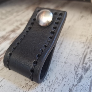 Könnte beinhalten: Schwarzer Leder-Schubladenzug mit einem silbernen Metallknopf und genähten Kanten.