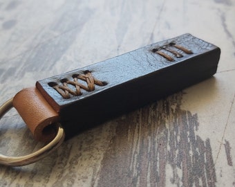 May include: A black leather keychain with a brown leather loop and a silver key ring. The leather is stitched with brown thread.