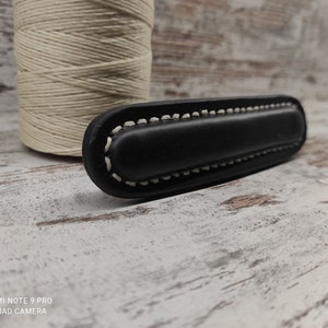 Op de afbeelding: Zwarte leren handgreep met witte stiksels. De handgreep is rechthoekig en heeft een licht afgeronde rand.