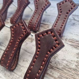 May include: Close-up of multiple brown leather drawer pulls with a diamond shape and stitched edges.