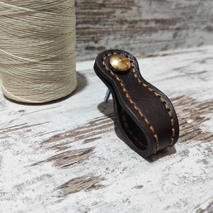 May include: A brown leather pull handle with a brass button and a light brown stitch detail.