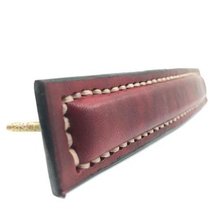 May include: A red leather drawer pull with a stitched border and a brass screw.