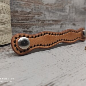 Peut inclure: Une sangle en cuir marron avec un design ondulé et deux boucles en métal argenté. La sangle est cousue avec un fil marron.