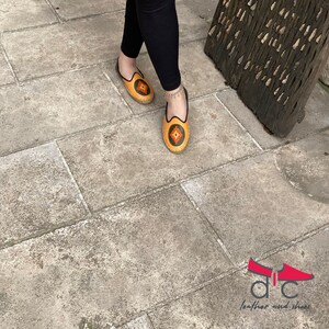 May include: A pair of yellow leather slippers with colorful embroidery. The slippers have a pointed toe and a flat sole.