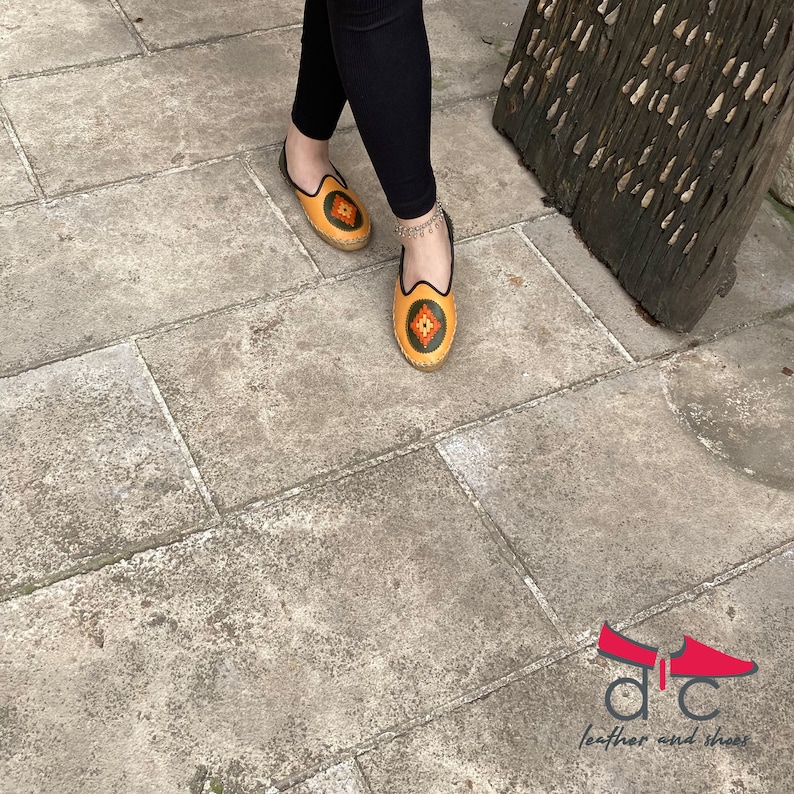 May include: A pair of yellow leather slippers with colorful embroidery. The slippers have a pointed toe and a flat sole.