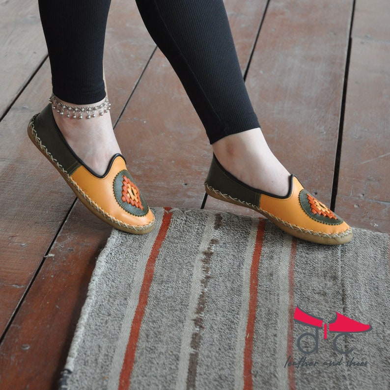 May include: A pair of orange and green leather slippers with a decorative embroidered design. The slippers are on a striped rug.