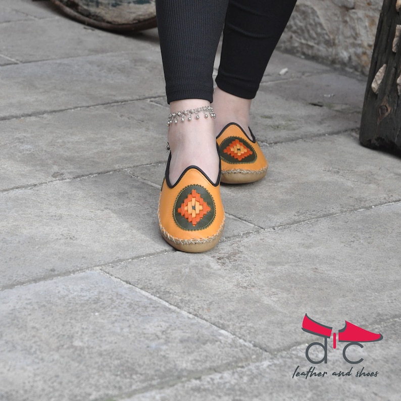 May include: A pair of yellow leather shoes with a geometric pattern on the toe. The shoes have a black trim and a brown sole.