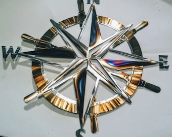 May include: A metal compass with a gold-toned outer ring and a silver-toned star-shaped compass rose. The compass points are labelled N, S, E, and W.