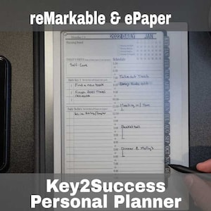 May include: A black and gray stylus rests on a white e-paper tablet with a daily planner displayed. The planner includes a section for "Self-Care" with tasks like "Find a new book" and "Finish 2021 Travel Receipts". The tablet is labeled "Key2Success Personal Planner" and has a calendar with the month of January 2022 visible.