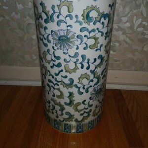 May include: A white ceramic umbrella stand with a green and blue floral pattern. The stand has a decorative border around the top.