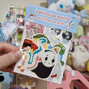 May include: A pack of stickers featuring characters from the film Spirited Away. The pack has a blue header with the words "bathhouse spirits sticker pack" in pink and white. The stickers include a dragon, a faceless spirit, and other characters.