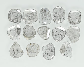 May include: A collection of 15 rough, clear, and translucent diamonds. The diamonds are various shapes and sizes, and they are arranged in a random pattern on a white background.