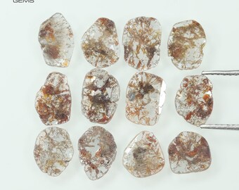 May include: Twelve rough, clear, and brown diamonds, some with inclusions, arranged in three rows of four. The diamonds are on a white surface.