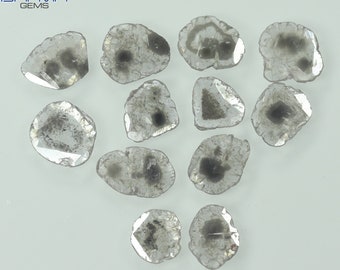May include: A collection of rough-cut, gray diamonds with dark inclusions. The gemstones are irregularly shaped, with a translucent appearance and a subtle sparkle. The diamonds are displayed against a white background, showcasing their natural beauty and unique characteristics.