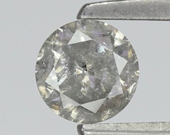 Puede incluir: Una piedra preciosa de diamante redonda, clara y gris, sostenida por unas pinzas.