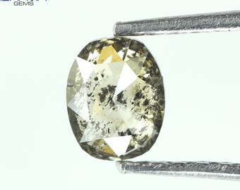 Puede incluir: Un diamante ovalado de color verde claro con inclusiones negras. El diamante está sujeto con unas pinzas.