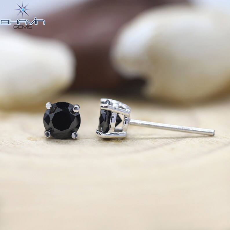 Pu&ograve; includere: Un paio di orecchini a perno con diamanti neri e montature in argento. Gli orecchini sono mostrati su una superficie di legno.