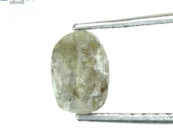 Puede incluir: Un diamante en bruto de forma ovalada, gris, sostenido por pinzas. El diamante tiene un acabado natural sin pulir.