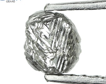 Puede incluir: Un diamante gris rugoso con muchas facetas, sostenido por unas pinzas. El diamante es una piedra preciosa en bruto sin cortar.