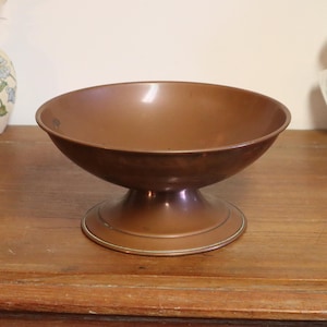 Peut inclure: Un bol sur piédestal de couleur cuivre avec un large bassin peu profond. Le bol repose sur une base arrondie avec un petit pied circulaire. L'intérieur du bol a une surface réfléchissante. Objet décoratif pour la maison.