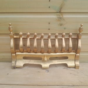 Peut inclure: Une grille de foyer dorée avec un design décoratif. La grille présente des barres verticales et des ornements décoratifs. La grille métallique a un aspect vintage et est probablement en fonte ou en matériau similaire.