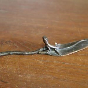 Può includere: Cucchiaio in metallo argentato fatto a mano con una coppetta a forma di foglia e un manico a forma di ramo. Il cucchiaio presenta una piccola figura dettagliata alla base della coppetta. Il cucchiaio è lungo circa 15 cm.