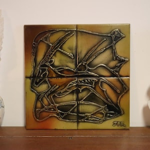 Op de afbeelding: Decoratieve opstelling met een keramische vaas met een veer, een vierdelig kunstwerk met een goud-zwart abstract ontwerp en een witte buste. Het kunstwerk heeft een handtekening rechtsonder.