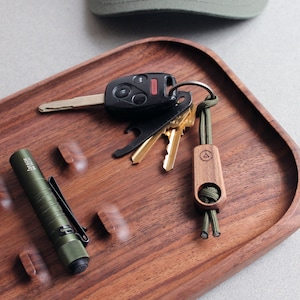 May include: A wooden tray with a green flashlight, a set of keys with a key chain, and a small wooden key holder with a green cord.