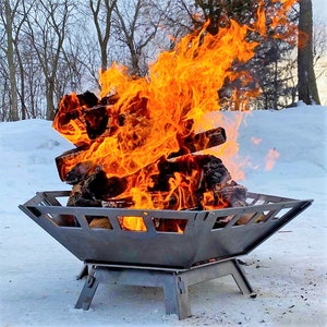 May include: A metal fire pit with a square base and a rectangular fire bowl. The fire pit is filled with burning logs and flames are rising from the fire pit. The fire pit is sitting on a snowy surface.