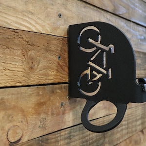 May include: Black metal bike rack with a cut-out silhouette of a bicycle. The rack is mounted on a wooden wall.