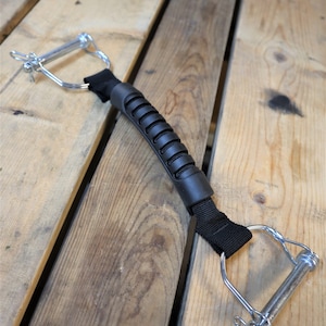 May include: A black strap with a rubber handle and two silver metal clips. The strap is attached to the clips with a loop.