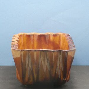 May include: A brown ceramic planter with a wavy, fluted design. The planter is rectangular in shape and has a glossy finish.