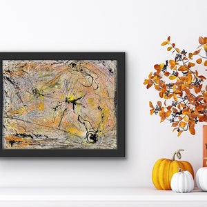 May include: Abstract art painting in a black frame. The artwork features a mix of colours, including orange, yellow, grey, and black, with splatters and lines. The painting is displayed on a white surface, with pumpkins and autumn foliage in the background.