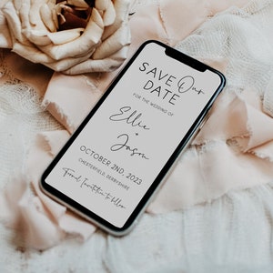 Könnte beinhalten: Ein Smartphone-Mockup mit einer Save-the-Date-Ankündigung für die Hochzeit von Ellie und Jason am 2. Oktober 2023 in Chesterfield, Derbyshire. Das Telefon liegt auf einem weißen und rosafarbenen Stoffhintergrund mit einer beigefarbenen Rose.