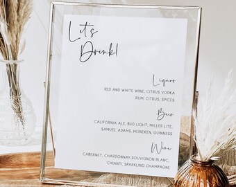May include: A framed sign with the text "Let's Drink!" and a list of drinks, including liquor, beer, and wine. The sign is sitting on a wooden surface with a brown vase and a beige cloth.