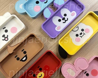 May include: A collection of colorful, rectangular pencil cases with cartoon character designs. The cases are in various colors, including blue, purple, yellow, brown, red, white, and pink. Each case features a different character face with black, pink, and white accents.
