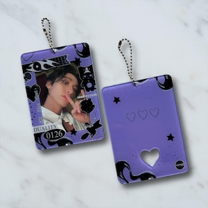 May include: Two rectangular, purple keychains with silver chain attachments. One keychain features a photo of a person, black and white graphics, and the text "DUALITY 0126". The other has hearts, stars, and a heart-shaped cutout.