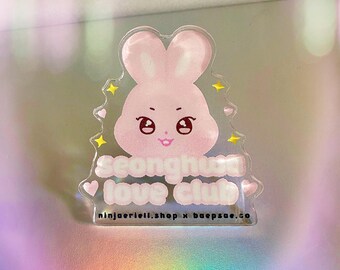 Pode incluir: Um pingente de acrílico transparente com um design de coelho rosa e o texto "Seonghwa love club". O pingente inclui corações e estrelas, com o endereço do site ninjaeriell.shop x baepsae.co.