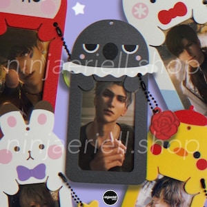 May include: A collection of five vertical card holders featuring cartoon character designs in red, white, black, and yellow. Each holder displays a portrait of a person and includes a small charm, such as a red rose or yellow star, on a black ball chain.