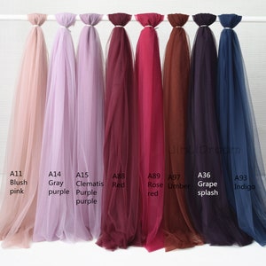 May include: Eight different colors of tulle fabric swatches, labeled with their color names and product codes. The colors are blush pink, gray purple, clematis purple, red, rose red, umber, grape splash, and indigo.