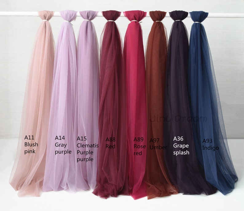 May include: Eight different colors of tulle fabric swatches, labeled with their color names and product codes. The colors are blush pink, gray purple, clematis purple, red, rose red, umber, grape splash, and indigo.