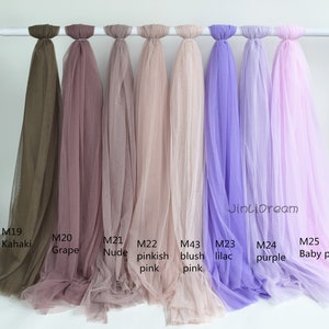 May include: Nine different colors of tulle fabric swatches hanging from a white rod. The colors are khaki, grape, nude, pinkish pink, blush pink, lilac, purple, and baby pink. The swatches are labeled with their corresponding color names and product codes.